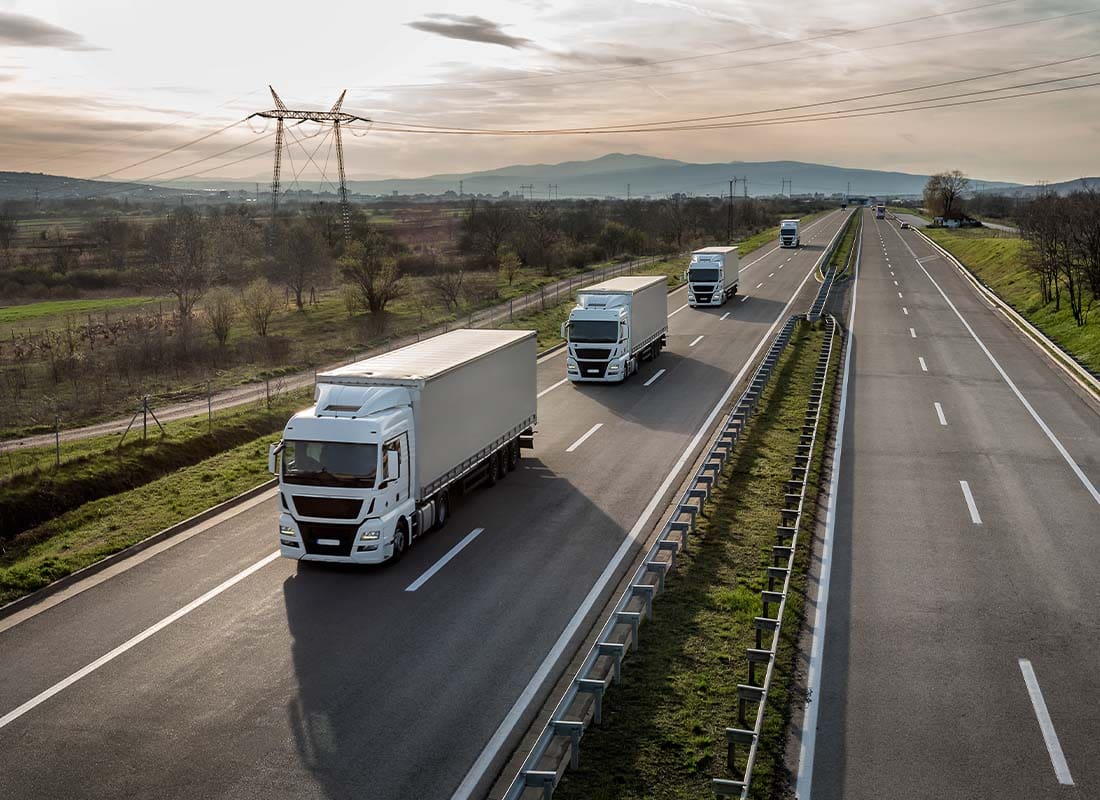 Transportation Insurance - Caravan or Convoy of a Fleet of Semi Trucks in a Line Along a Country Highway on Their Way to Deliver Goods at Dusk