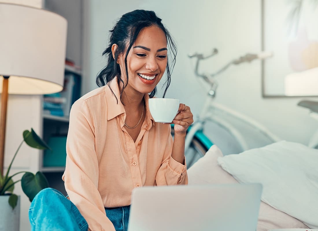 Blog - Cheerful Woman Sips on Coffee as She Reads on Her Laptop at Home